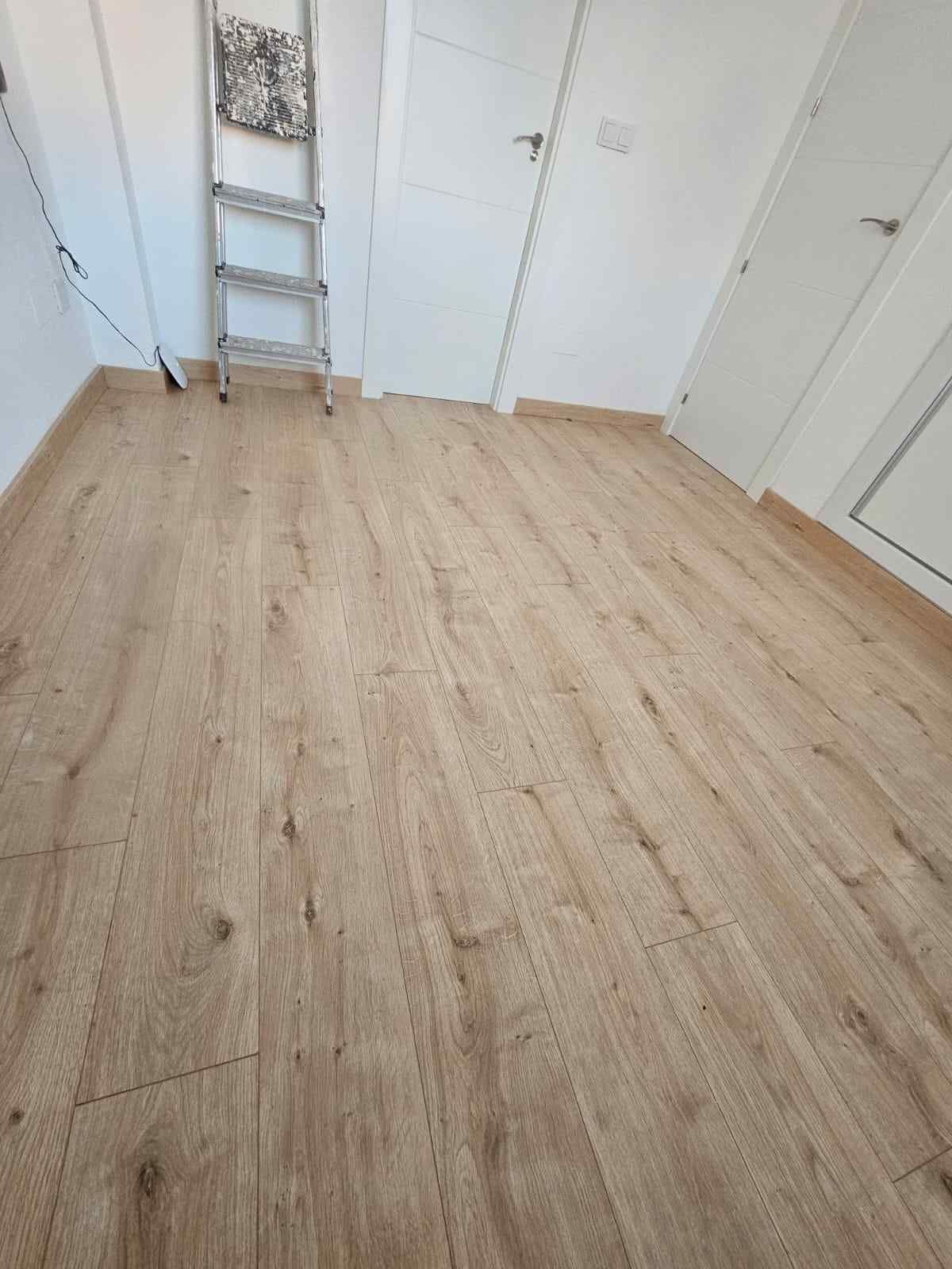 Habitación con suelo de imitación madera clara, paredes blancas, dos puertas y una escalera de mano.