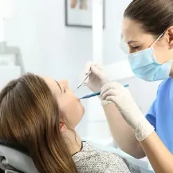 Dentista con mascarilla examinando los dientes de un paciente. Entorno clínico.