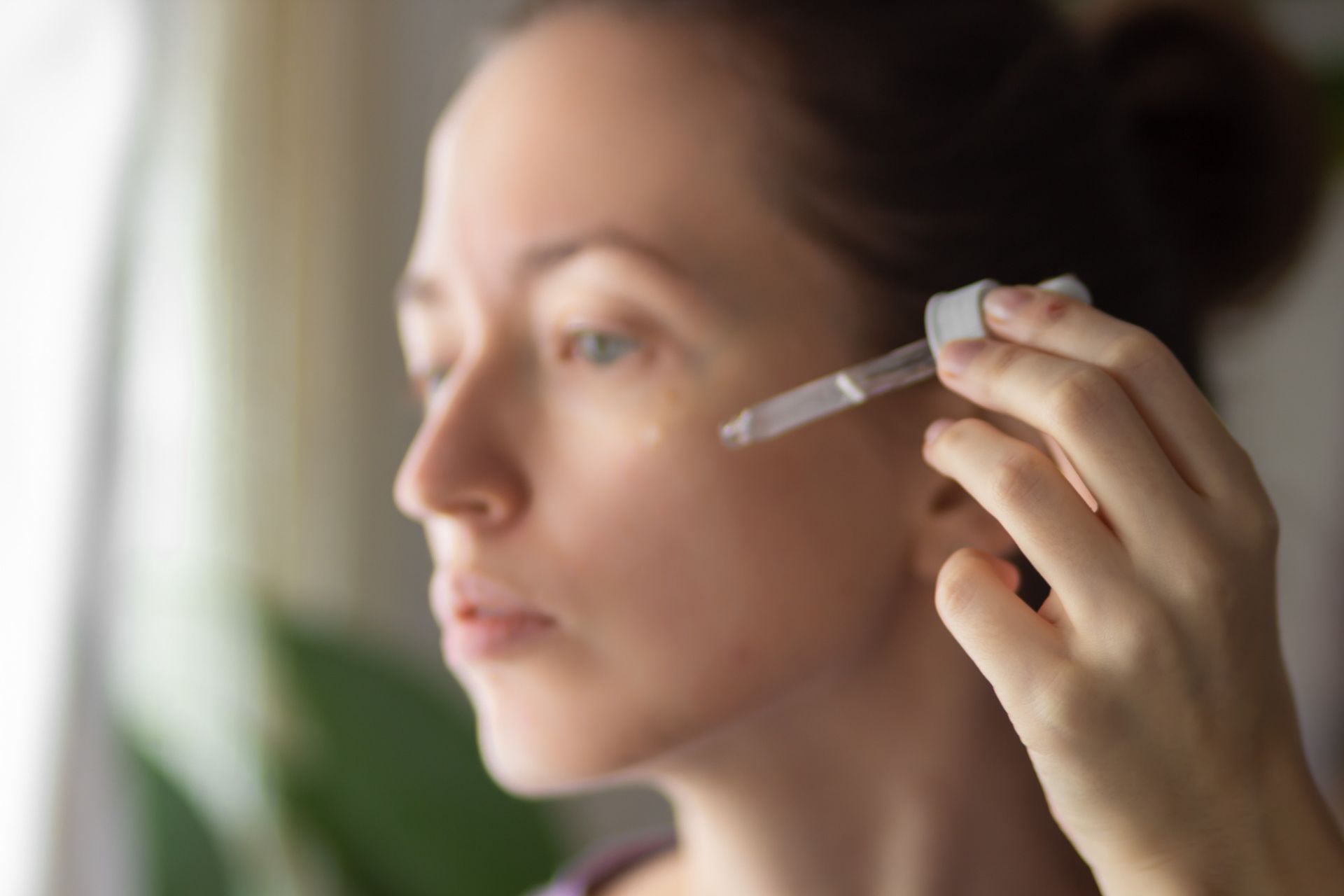 Mujer aplicándose suero para el cuidado de la piel en el rostro con un gotero, bajo luz natural.