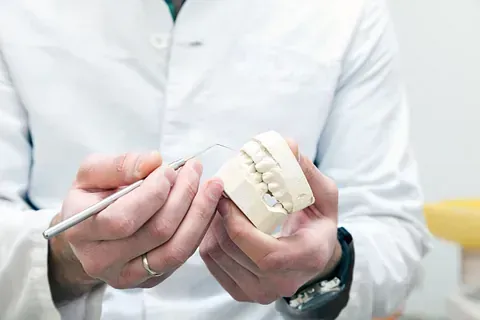 Un dentista con bata blanca examina un molde dental con un palillo de metal.