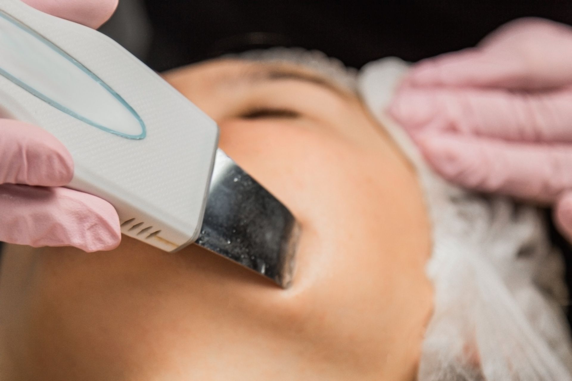 Persona que recibe un tratamiento facial con un dispositivo; esteticista con guantes rosas, primer plano.