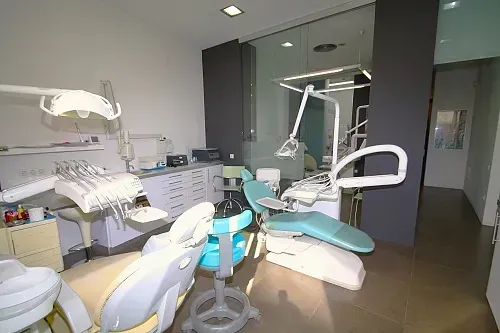 Interior del consultorio dental: sillón de dentista, equipamiento, armarios y mampara de cristal.
