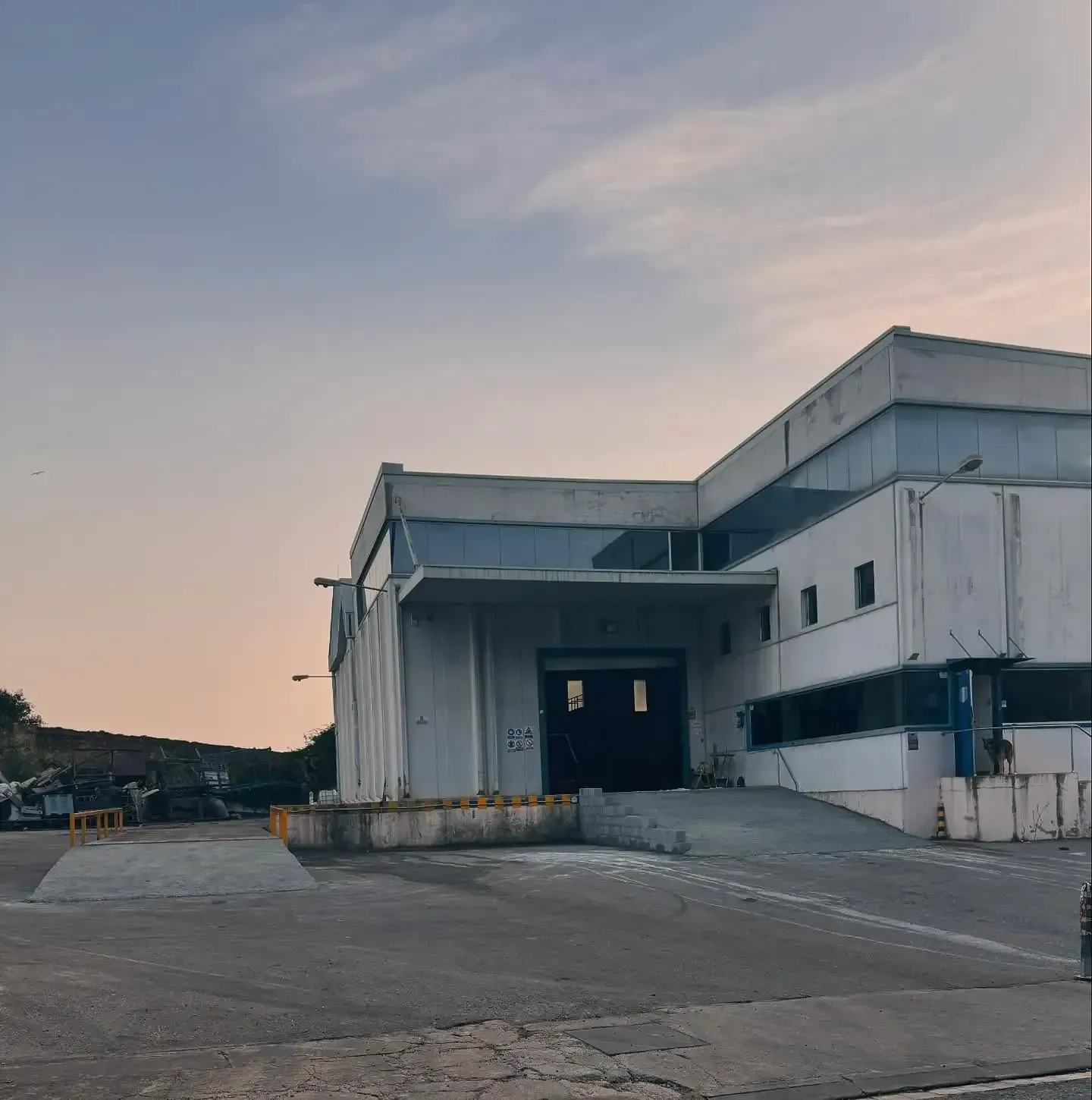 Un gran edificio industrial blanco con un muelle de carga bajo un cielo nublado.