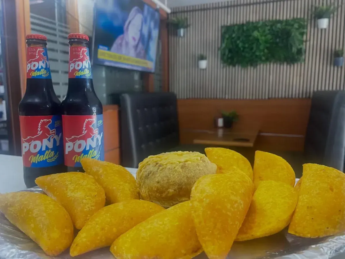 Bocadillos fritos amarillos sobre una mesa junto a dos bebidas embotelladas en el interior de un restaurante.