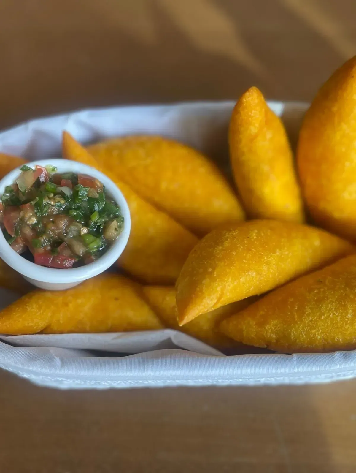 Bandeja de empanadas doradas fritas con una pequeña taza de salsa verde.
