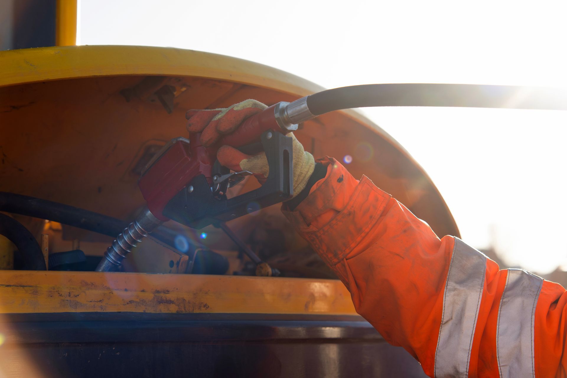 Une personne portant un gilet orange haute visibilité utilise un pistolet de remplissage de carburant pour alimenter un engin de chantier lourd.