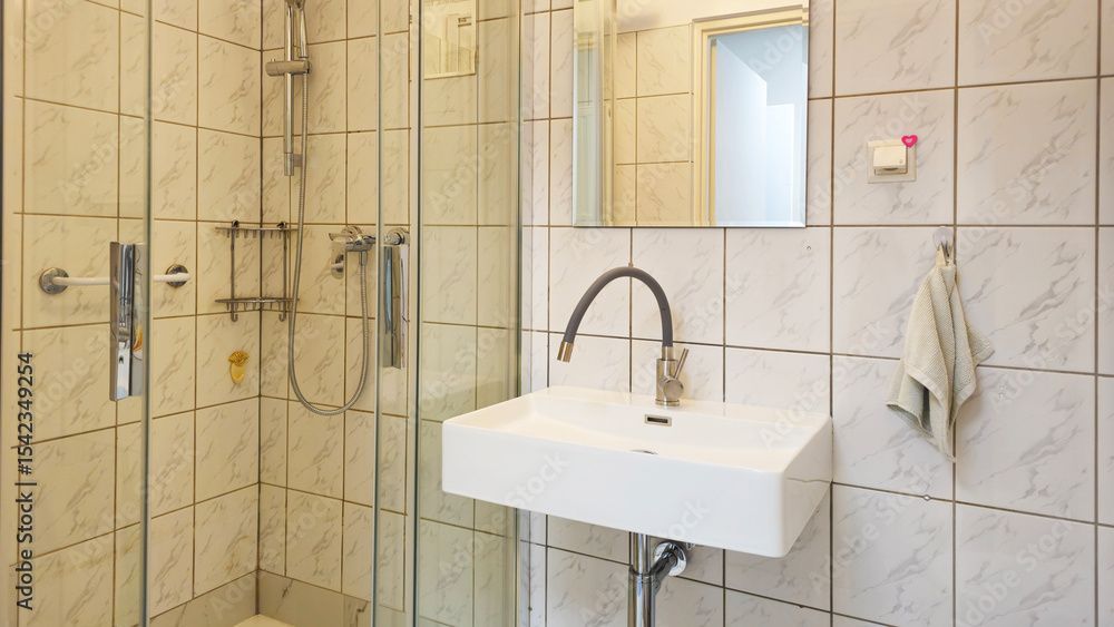 Salle de bain accessible avec douche carrelée, lavabo mural, miroir et porte-serviettes