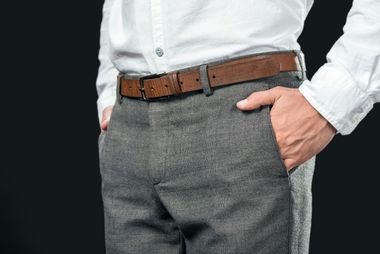 Un hombre que lleva una camisa blanca y un cinturón marrón está de pie con las manos en los bolsillos.