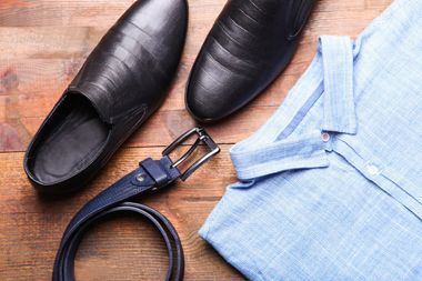 Un par de zapatos, un cinturón, una camisa y unos pantalones están sobre una mesa de madera.