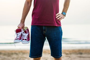 Un hombre sostiene un par de zapatillas rojas en la playa.