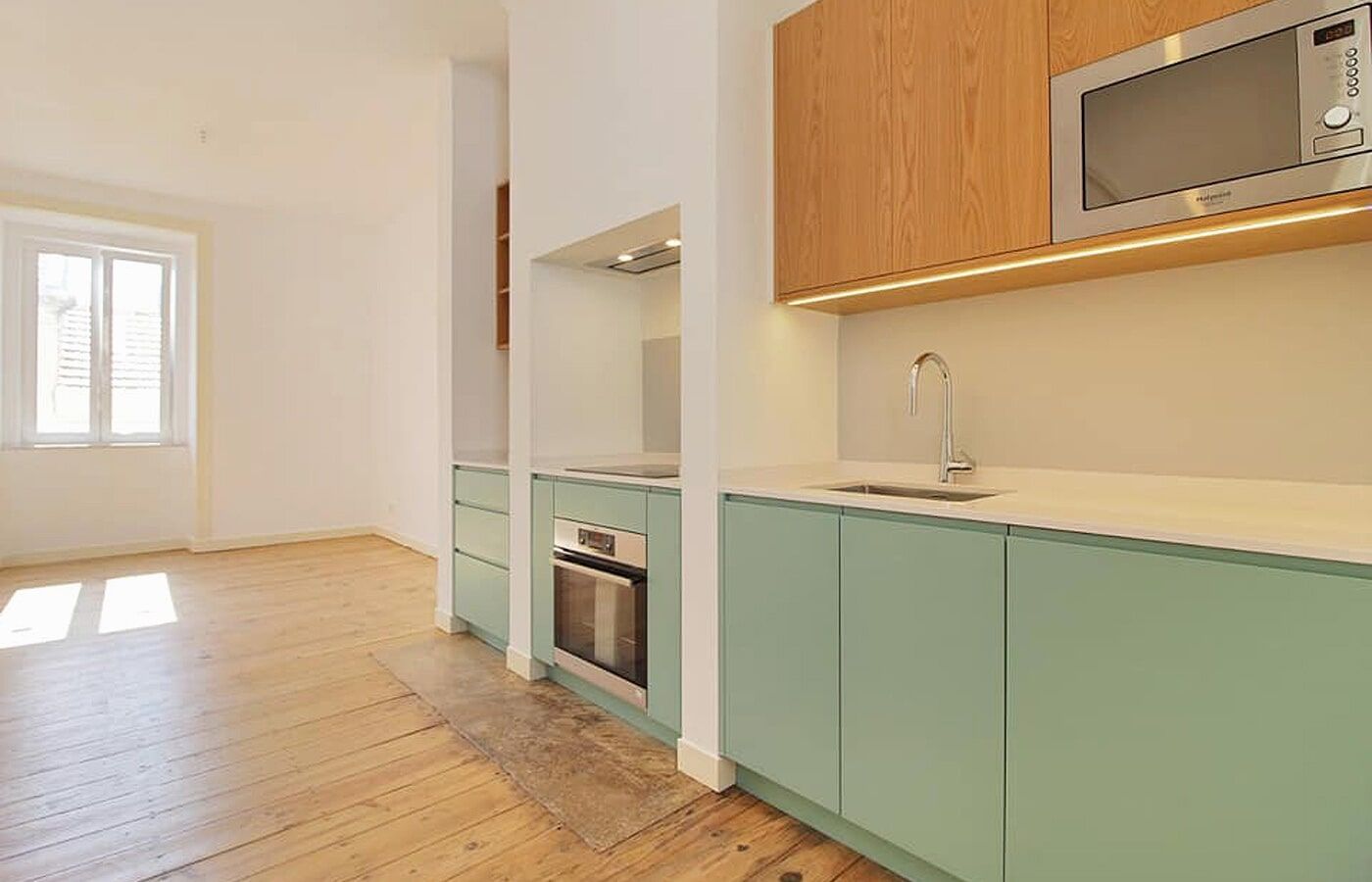 Cozinha com armários verde-claros, armários de madeira, eletrodomésticos de aço inoxidável e piso de madeira.