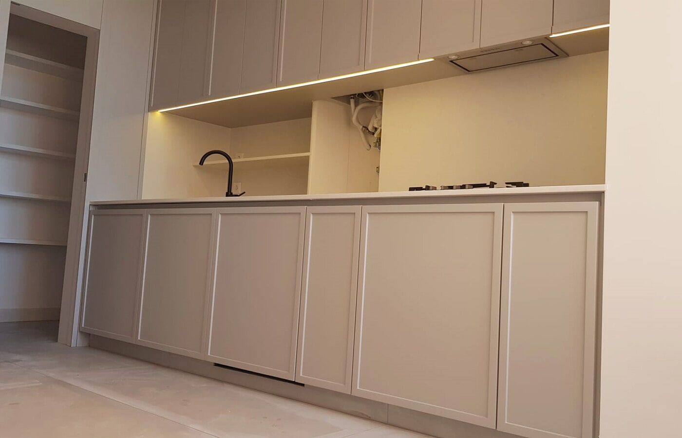 Cozinha moderna com armários cinza-claro, torneira preta e fogão embutido.