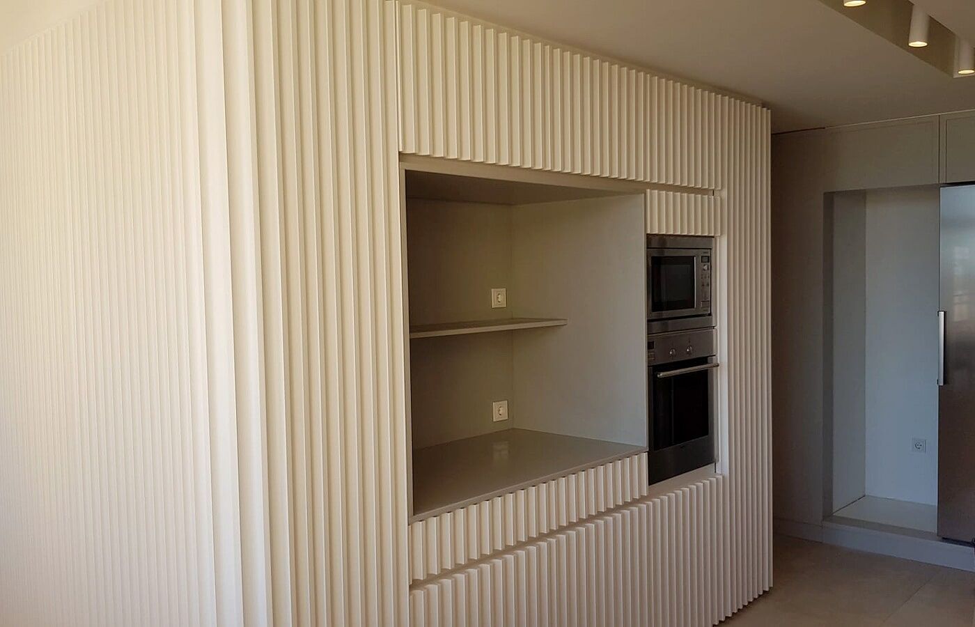 Armários de cozinha com textura vertical canelada, apresentando um nicho aberto com prateleiras e forno embutido.