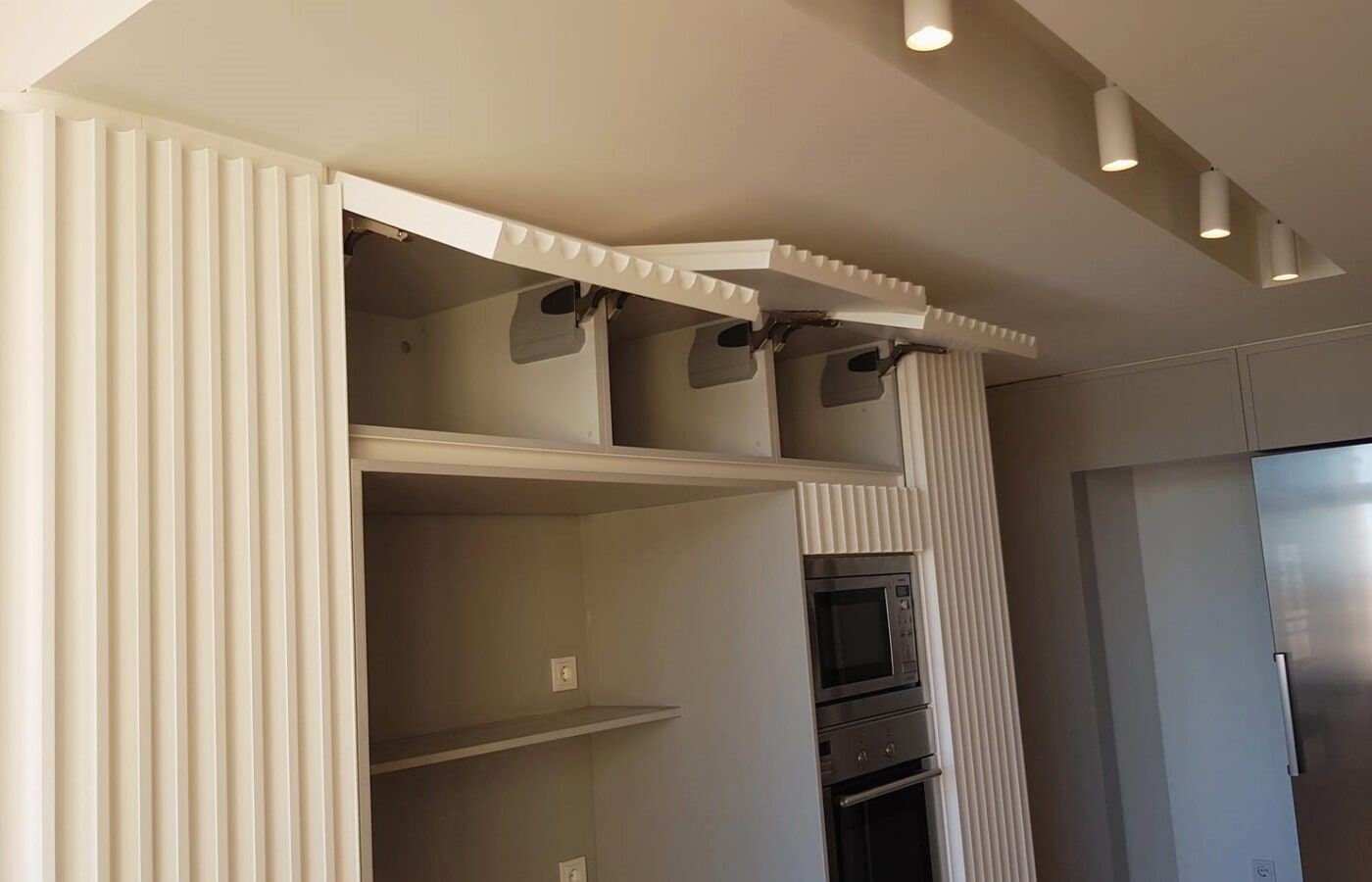 Armários de cozinha com portas superiores abertas, forno embutido e iluminação embutida.