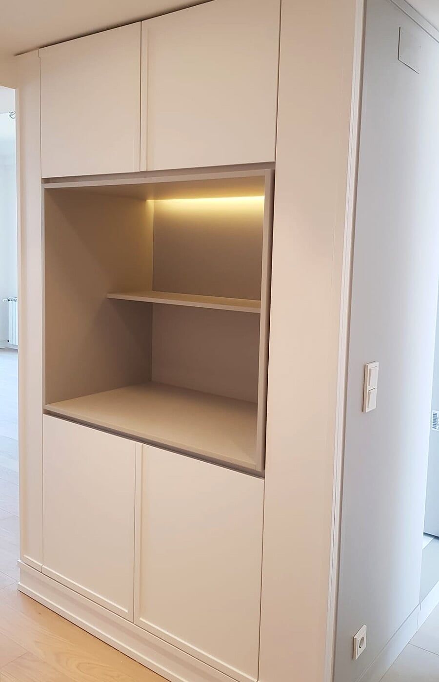 Móvel de arrumação embutido branco com prateleira rebaixada, iluminado por luz quente.