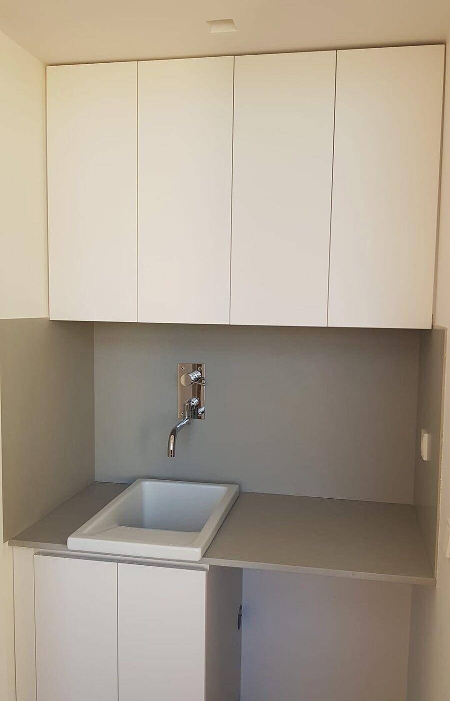 Área de lavanderia com armários brancos, bancada cinza e pia branca.