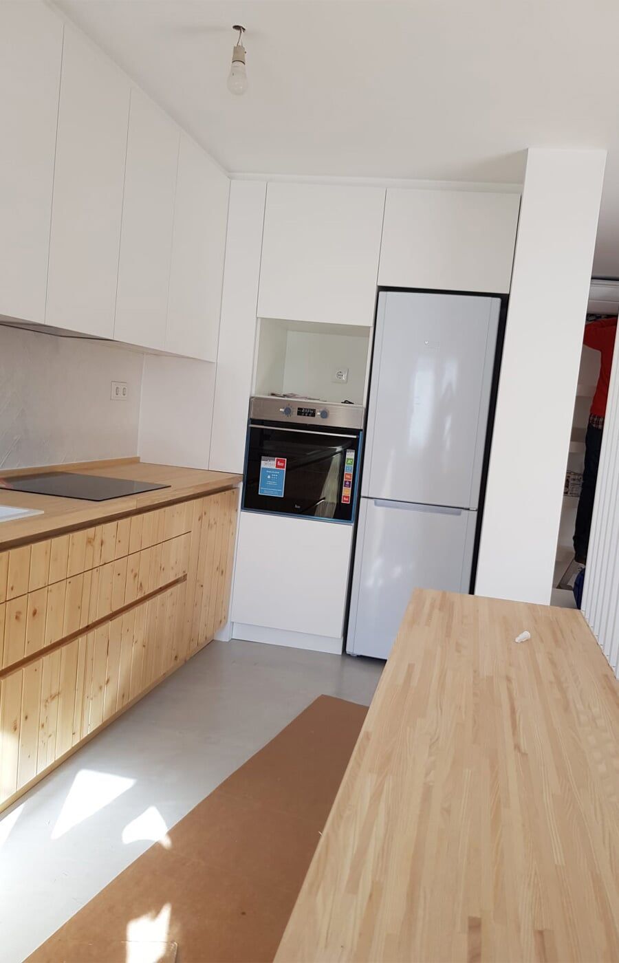 Cozinha moderna com armários de madeira clara, paredes brancas e geladeira.