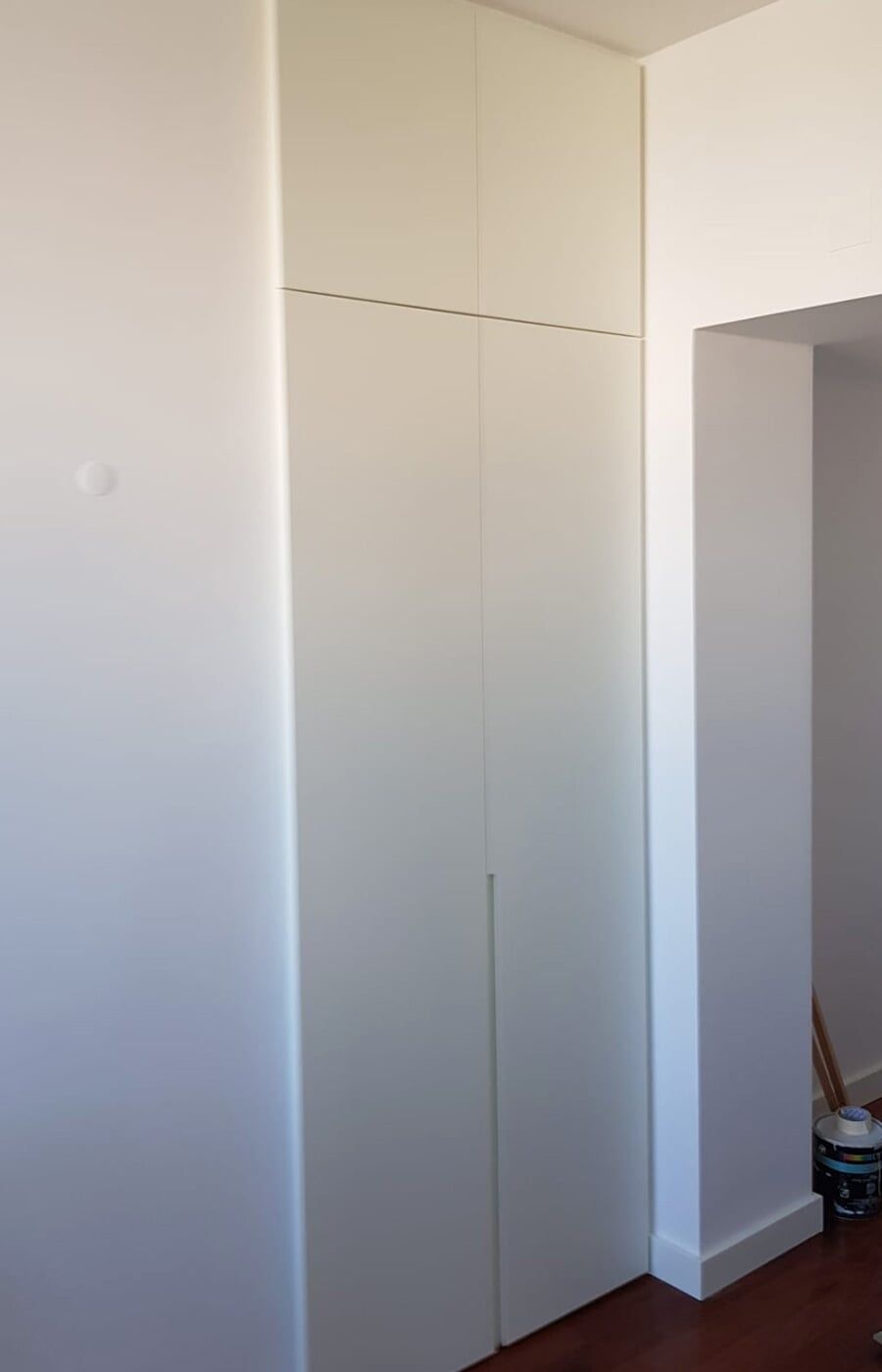 Armário embutido branco em um cômodo com paredes brancas e uma porta à direita.