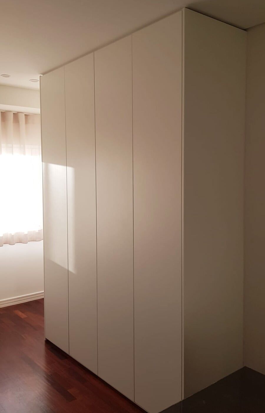 Armário embutido branco com seis portas. Piso de madeira escura à mostra.