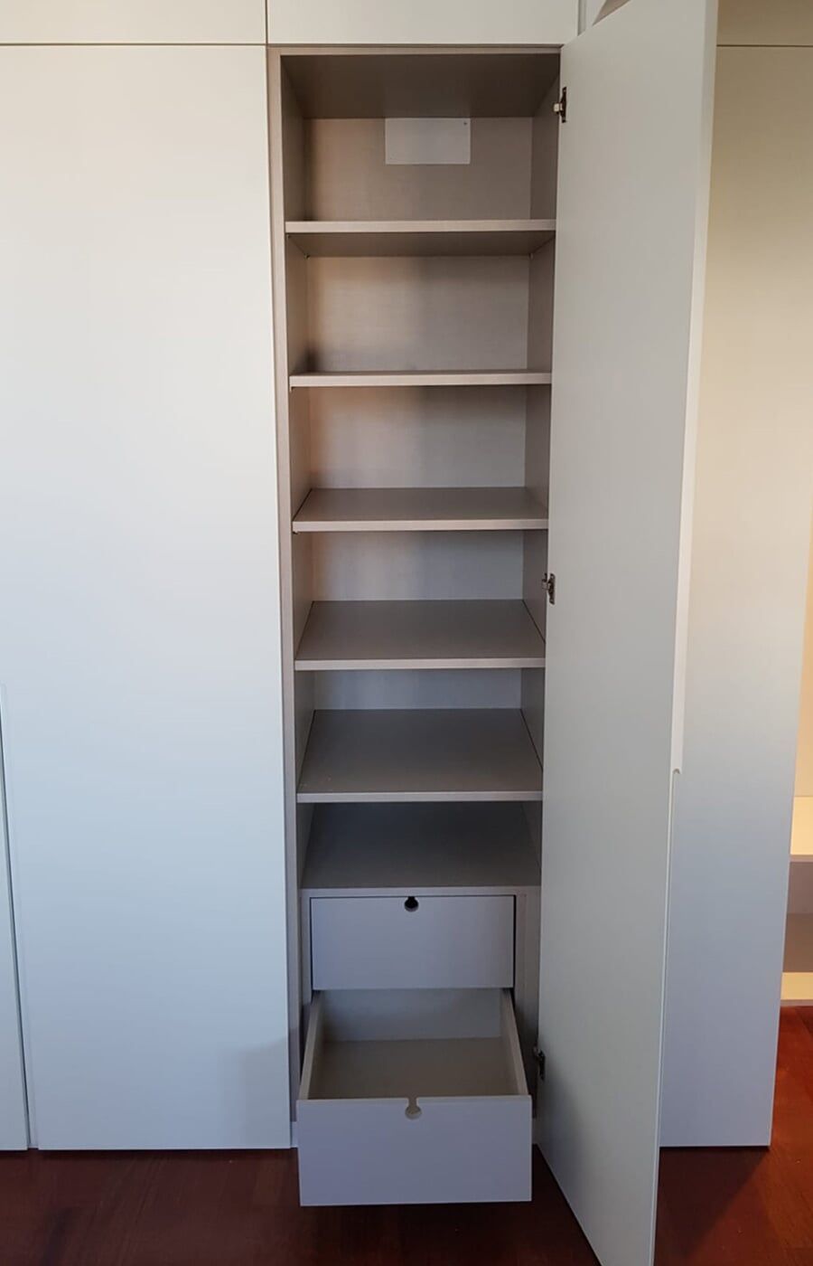 Armário de arrumação branco com porta aberta e prateleiras. A gaveta está aberta.