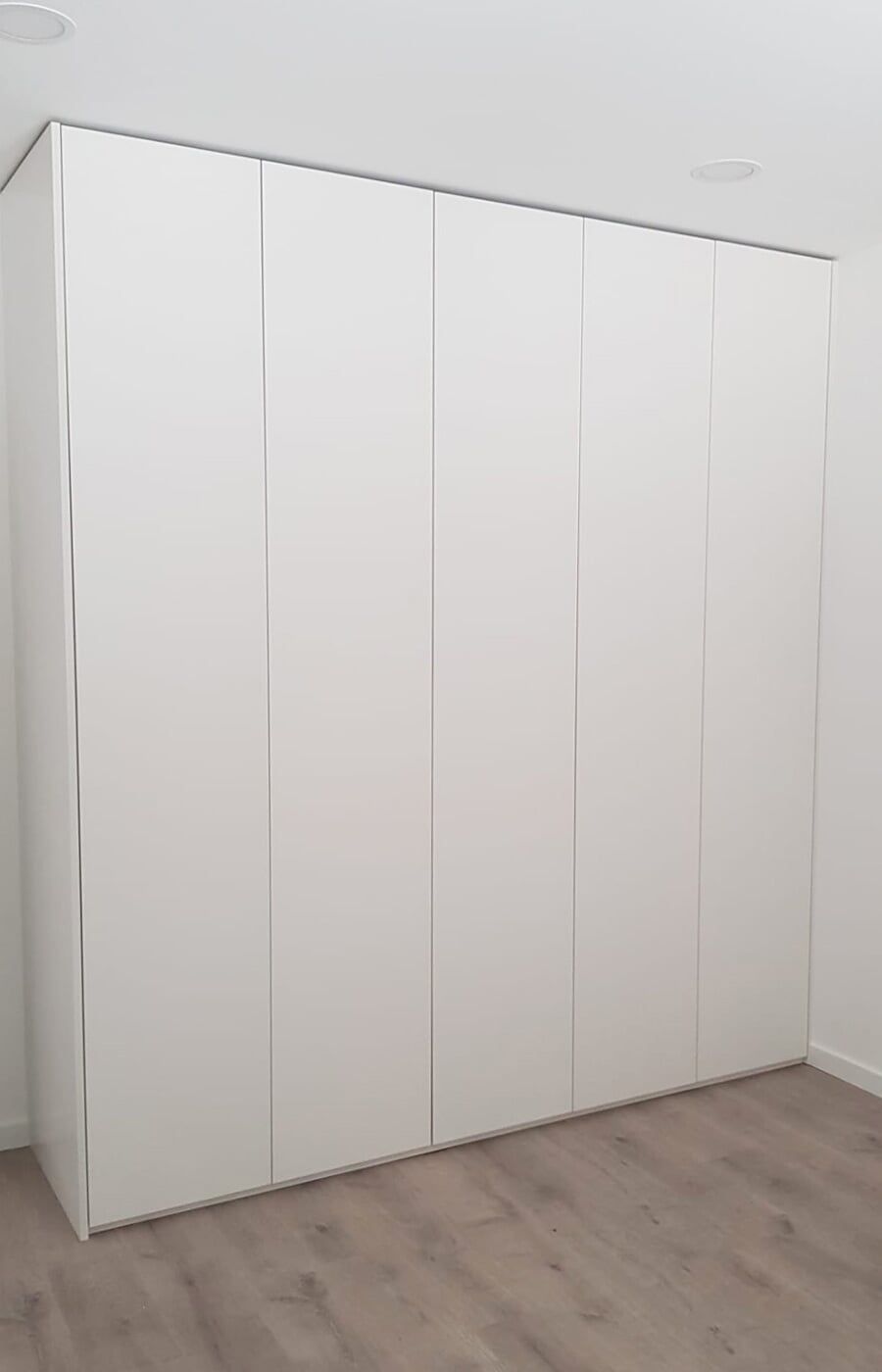 Armário embutido branco com seis portas em um quarto com piso de madeira clara.