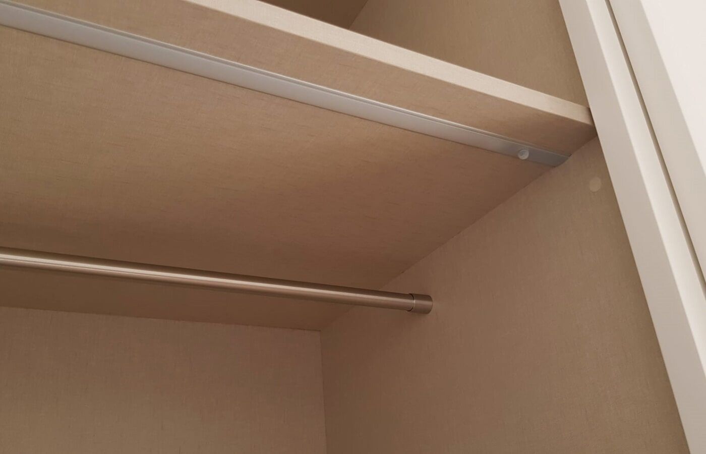 Interior de um armário com prateleira, varão e luminária. Estrutura de madeira em tons claros.