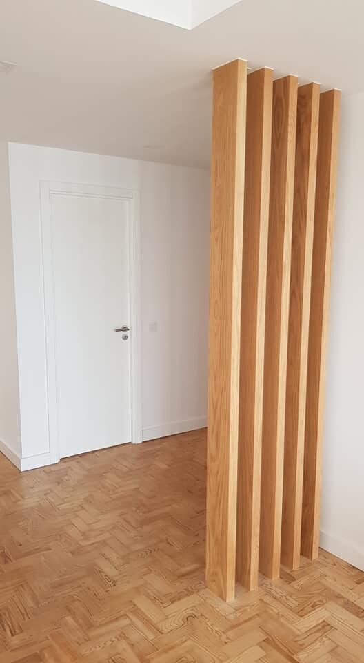 Divisória de ambiente com ripas de madeira em um cômodo com porta branca e piso de madeira.