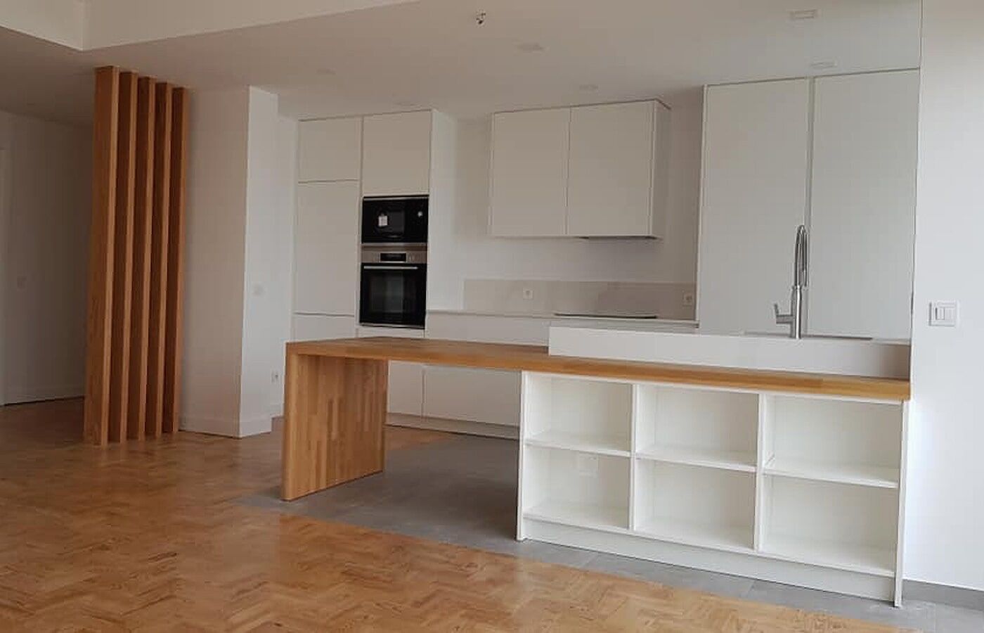 Cozinha moderna com armários brancos, ilha/mesa de madeira e parede com ripas de madeira.