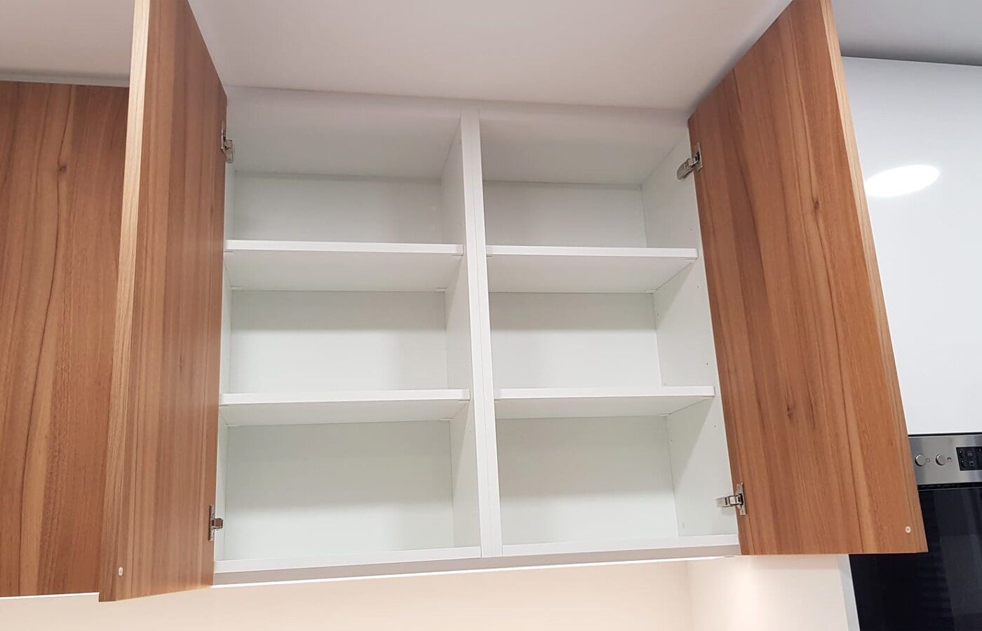 Armário de cozinha vazio com portas abertas em tom de madeira. O interior possui prateleiras brancas.