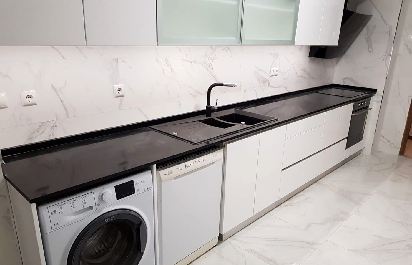 Cozinha moderna com bancadas pretas, armários brancos e eletrodomésticos embutidos.