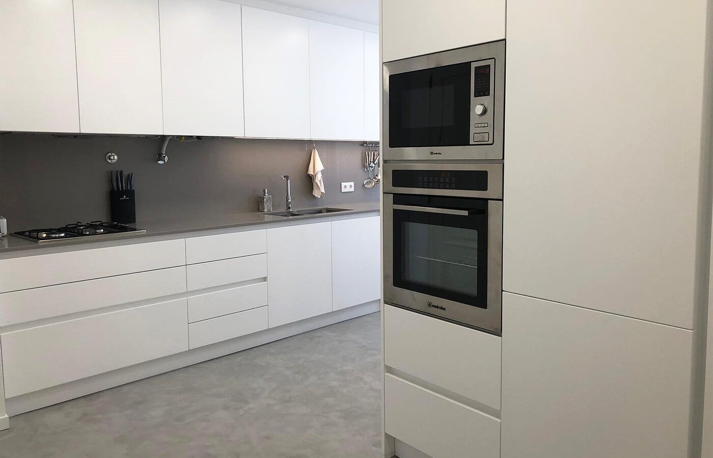 Cozinha moderna branca com micro-ondas, forno e armários embutidos. Bancada e backsplash cinza.