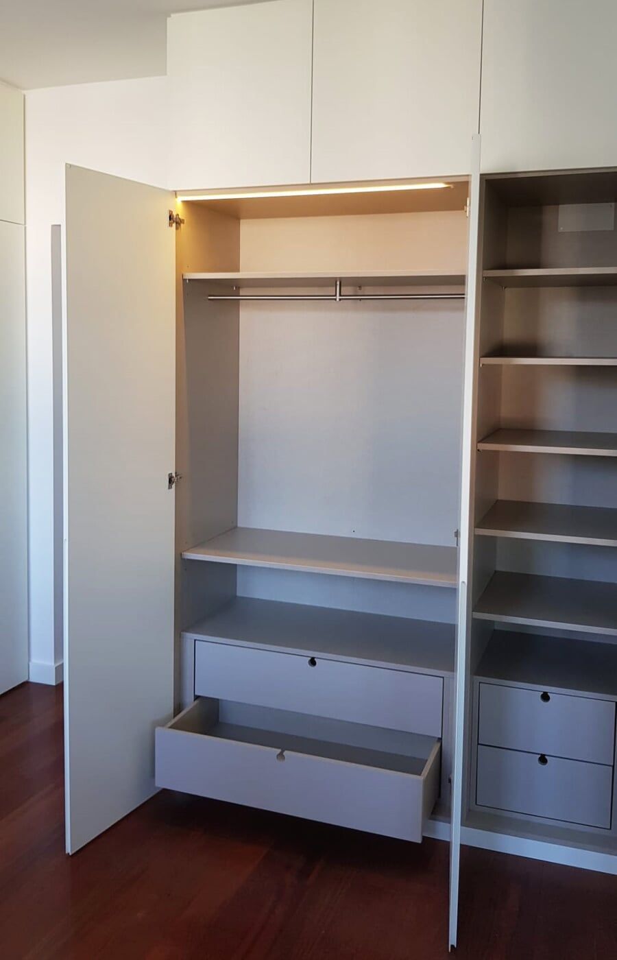 Armário embutido branco com porta aberta que revela prateleiras, gavetas e varão para pendurar roupas.