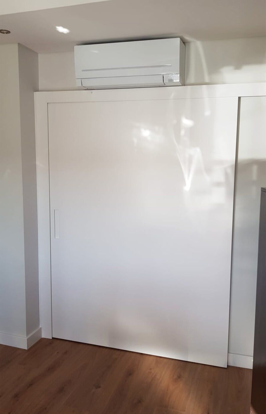 Parede branca brilhante com aparelho de ar condicionado instalado acima. Piso de madeira.