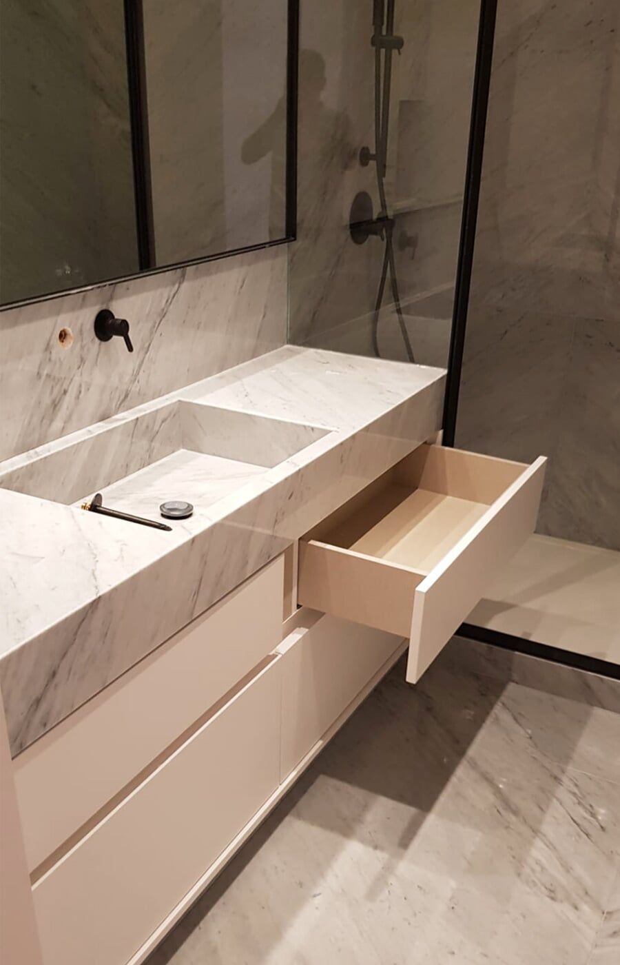 Banheiro moderno com bancada de mármore, gaveta aberta e box de chuveiro.