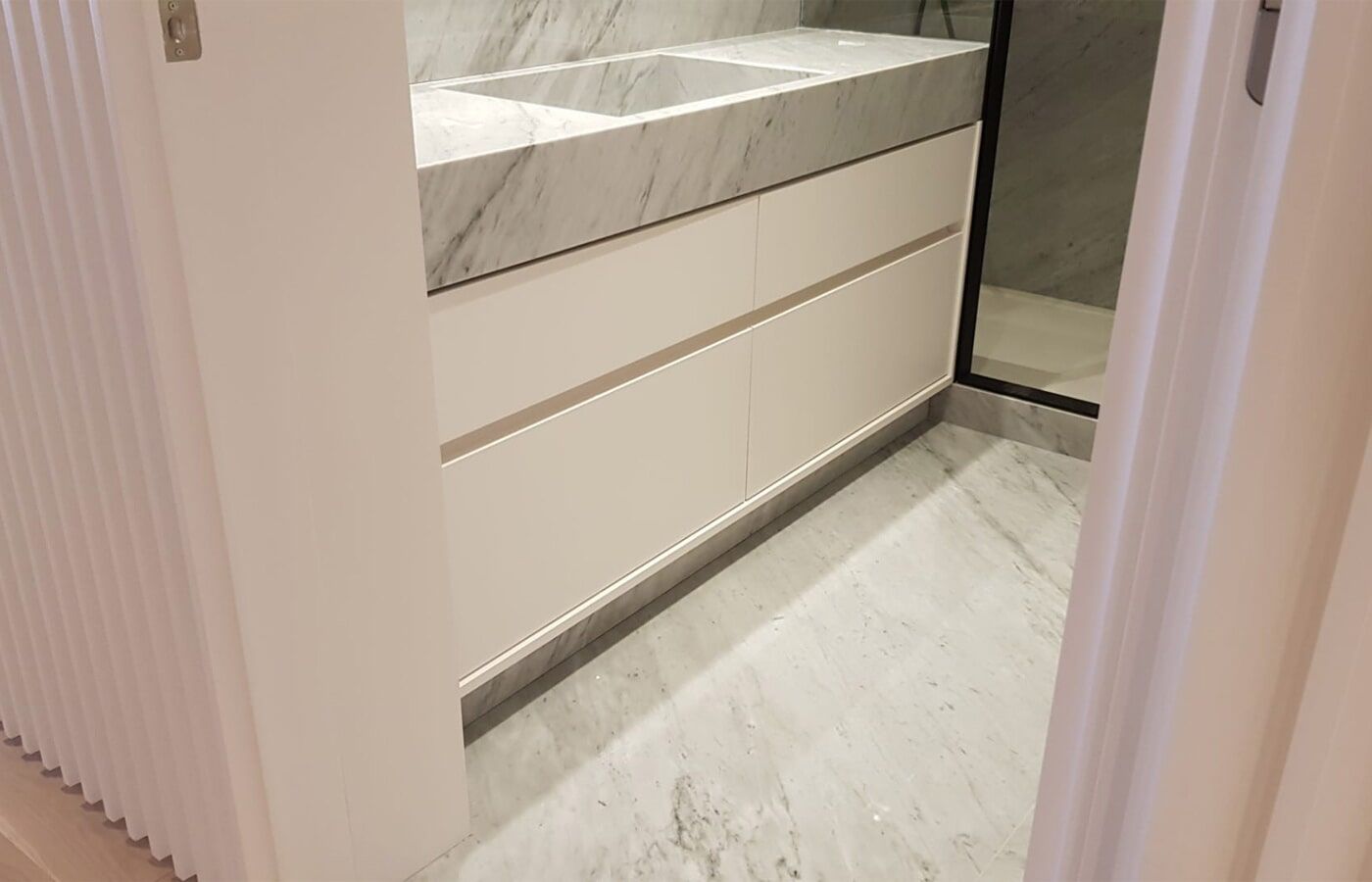 Armário de banheiro branco com tampo de mármore, duas cubas e três gavetas. Piso de azulejo cinza claro.