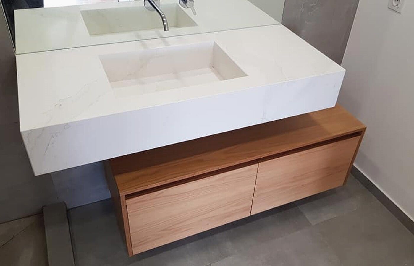 Lavatório retangular branco sobre armário de madeira com duas portas. Piso e parede cinza.