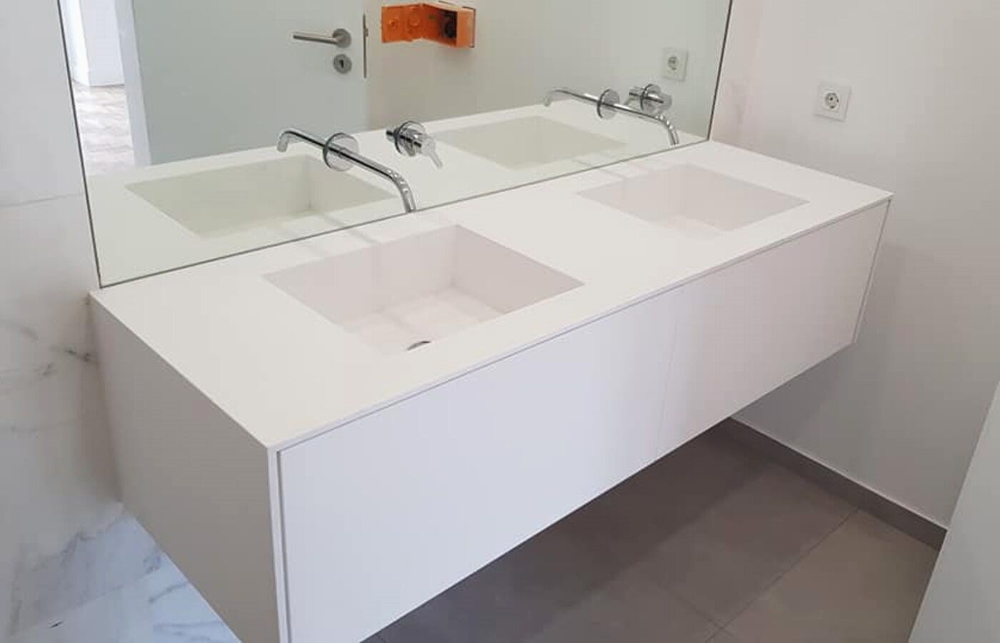 Pia dupla suspensa branca em um banheiro moderno com um grande espelho e torneiras cromadas.