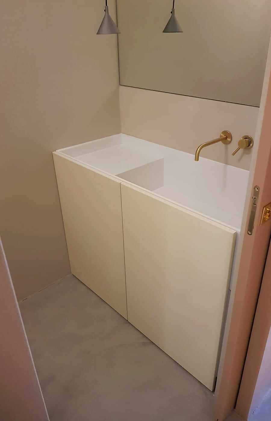 Bancada de banheiro cor creme com torneira dourada. A parede é bege claro com um espelho acima. 