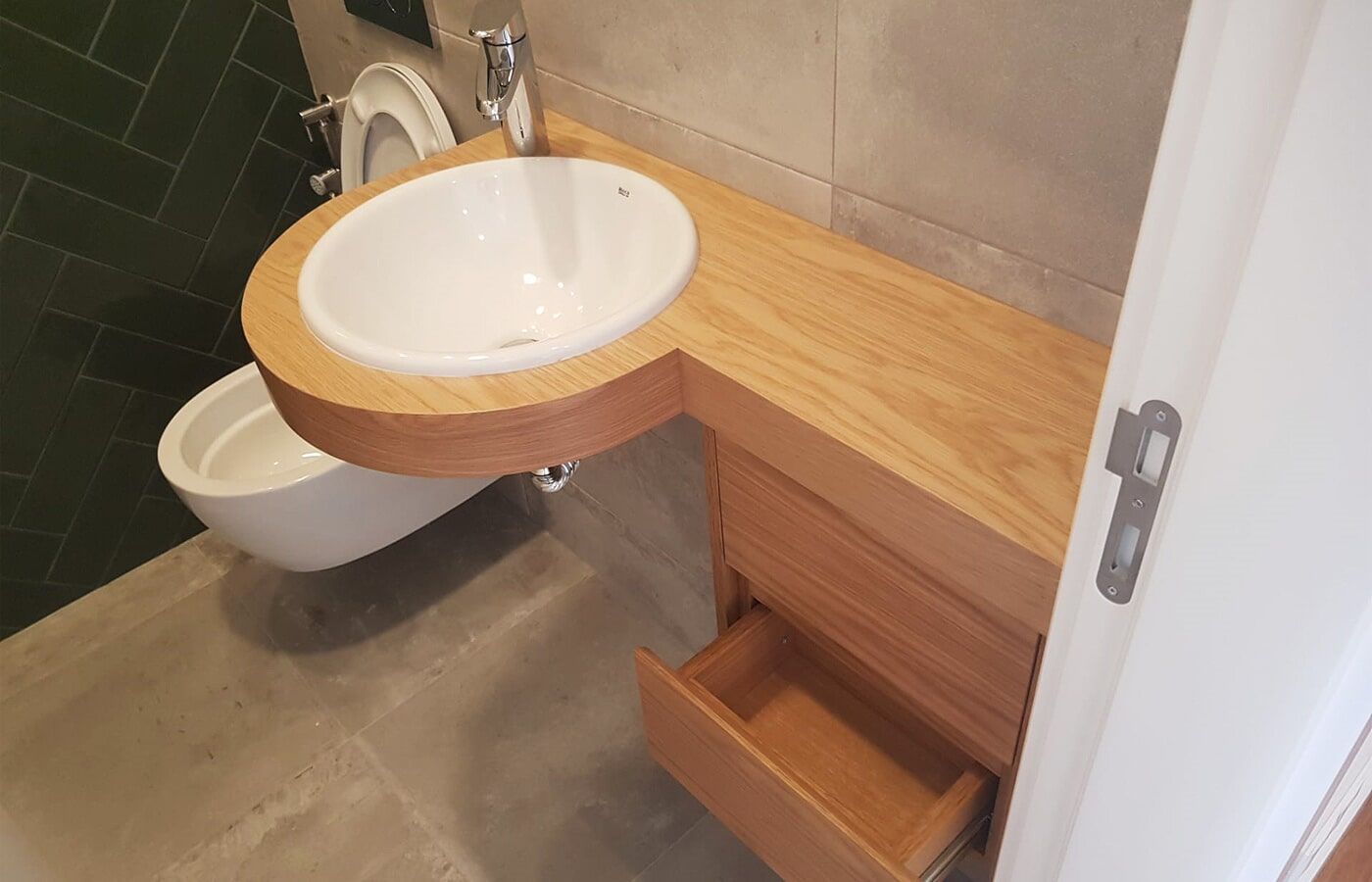 Banheiro com toucador de madeira, pia redonda, gaveta aberta e vaso sanitário suspenso.