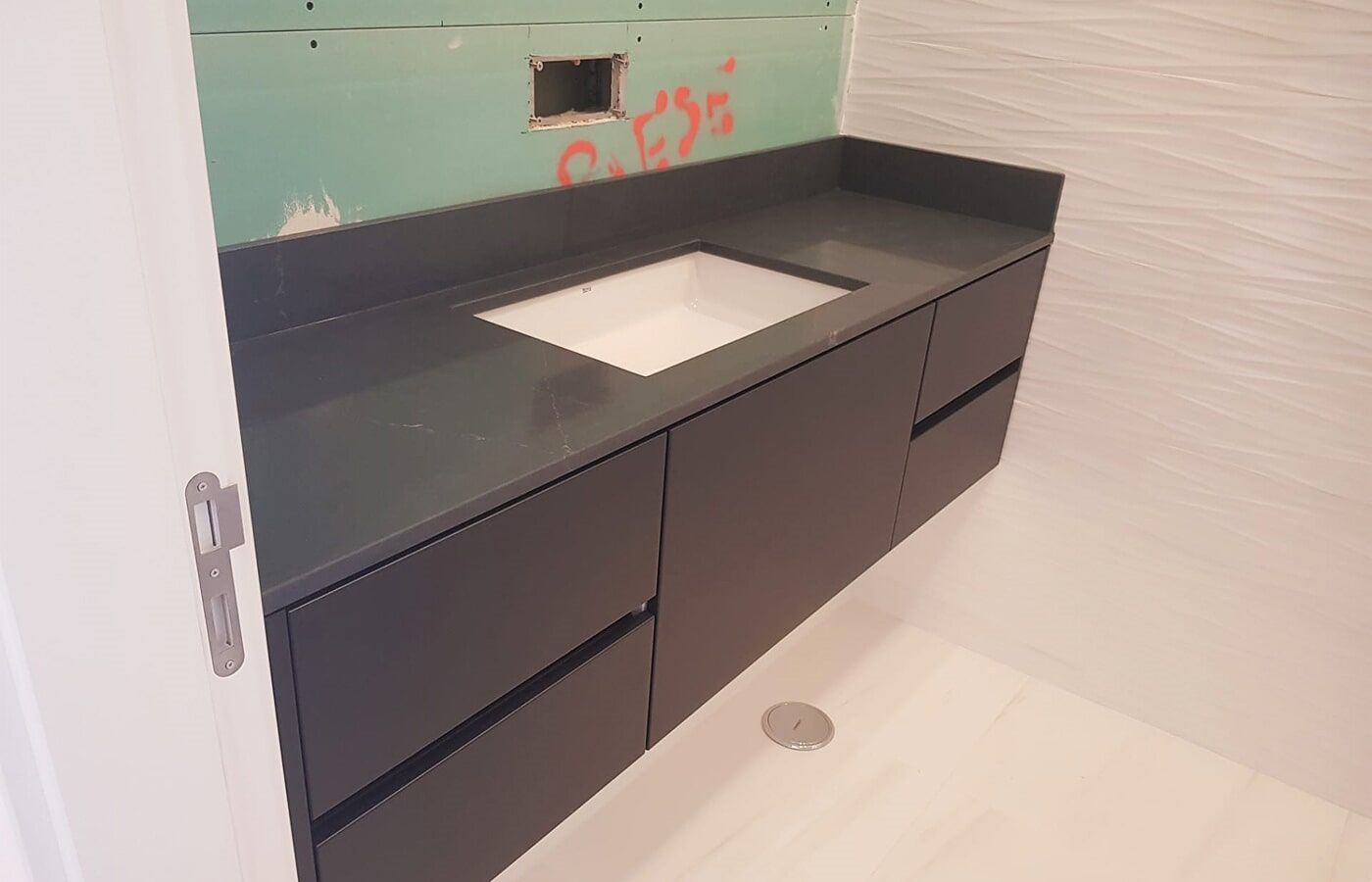 Móvel de banheiro suspenso cinza escuro com pia retangular branca e bancada.