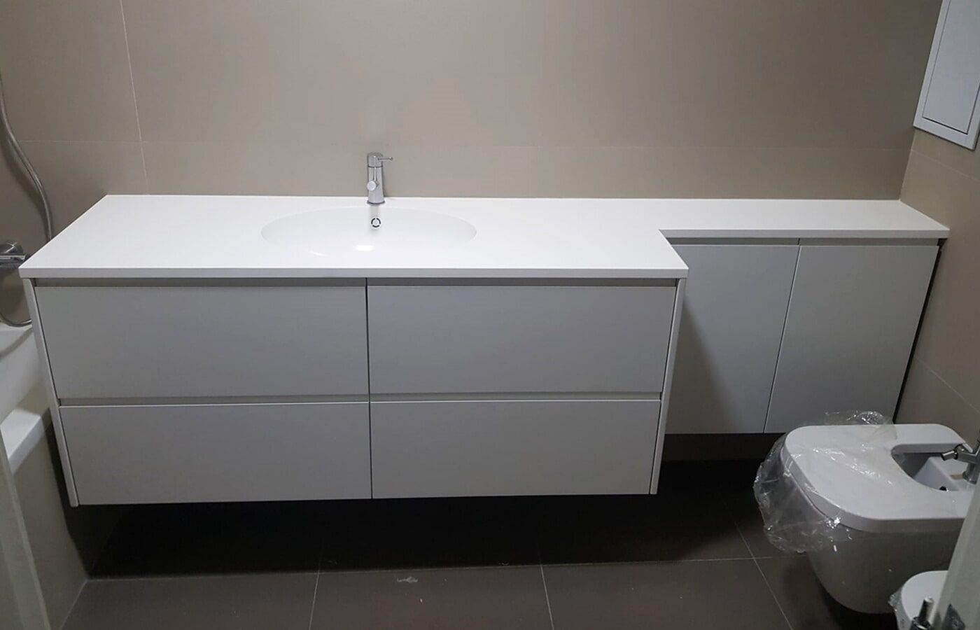 Banheiro moderno com bancada suspensa branca, pia e armário ao lado do vaso sanitário.