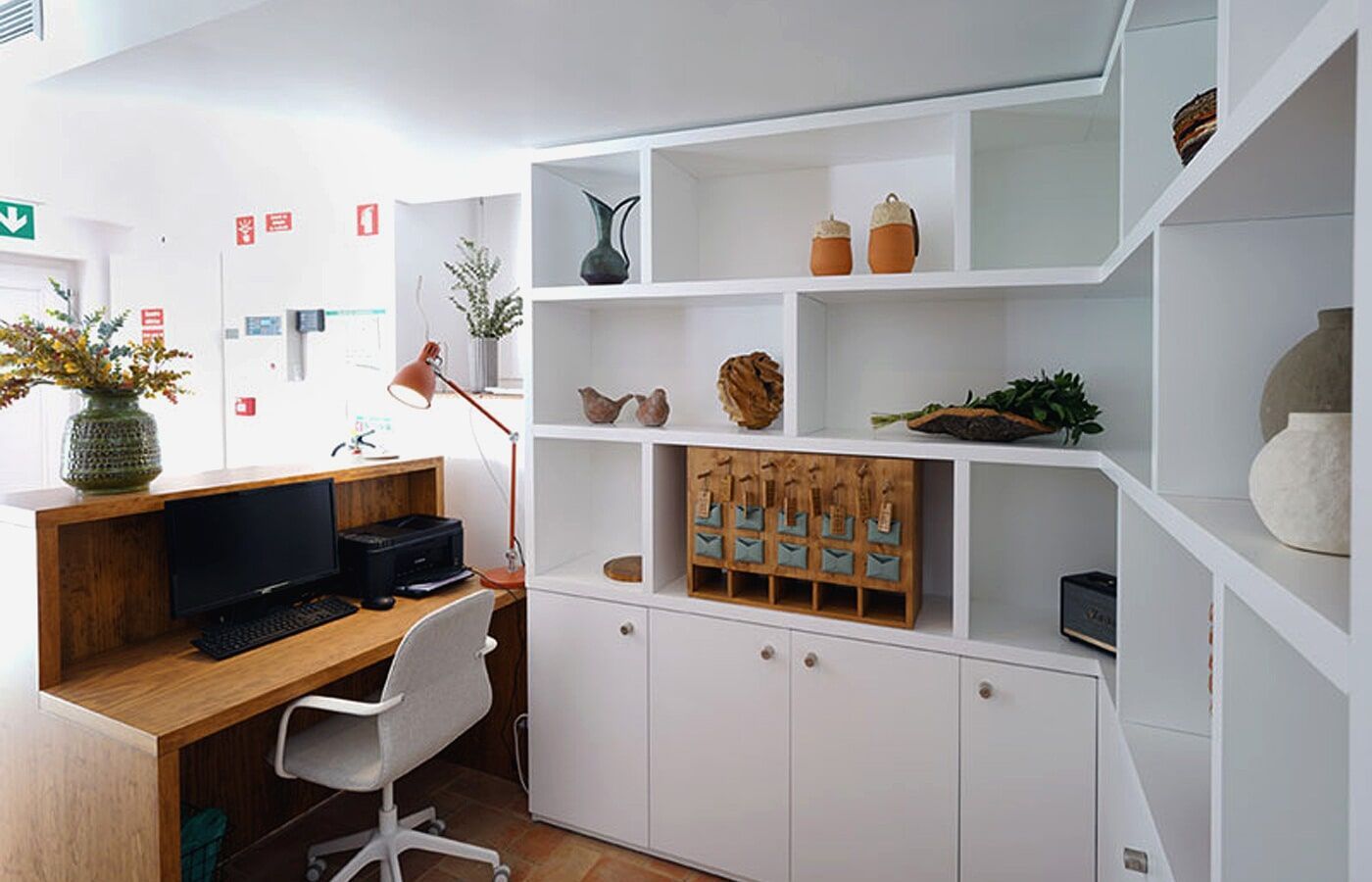 Balcão de recepção com prateleiras brancas embutidas, balcão de madeira, computador e cadeira de escritório.