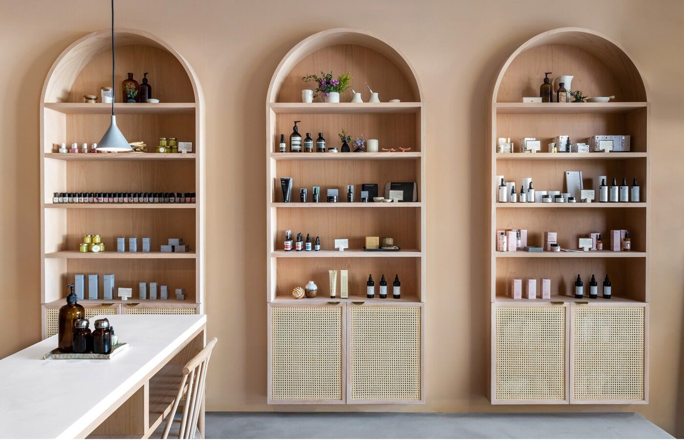 Três prateleiras arqueadas exibindo produtos de beleza em um espaço comercial de tons claros.