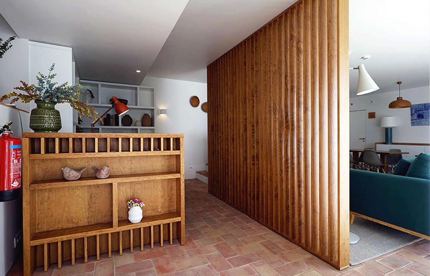 Prateleiras de madeira,  e uma divisória de madeira com nervuras separam o hall de entrada da sala de estar.