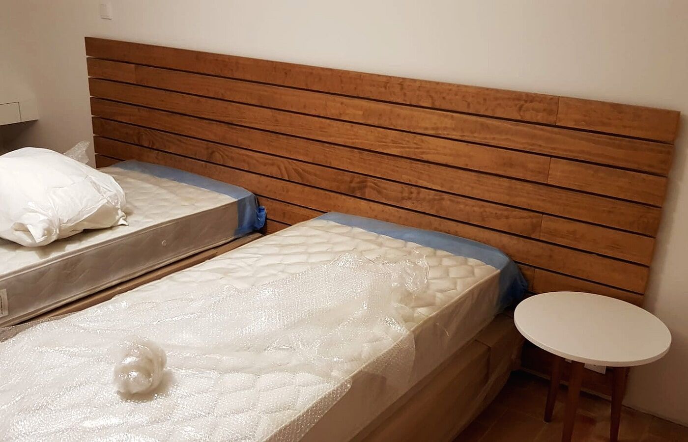 Duas camas de solteiro com cabeceira de madeira e uma pequena mesa de cabeceira branca.