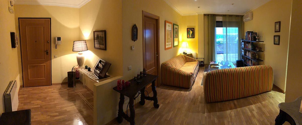 Sala de estar con paredes amarillas, piso de madera, dos sofás, puerta y ventanas.