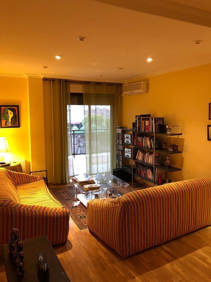 Sala de estar con paredes amarillas, sofás a rayas de color naranja, una estantería y una puerta corrediza de vidrio que da a un balcón.