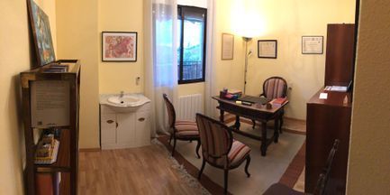 Una oficina acogedora con un escritorio, dos sillas y un lavabo junto a una ventana. Paredes amarillas.