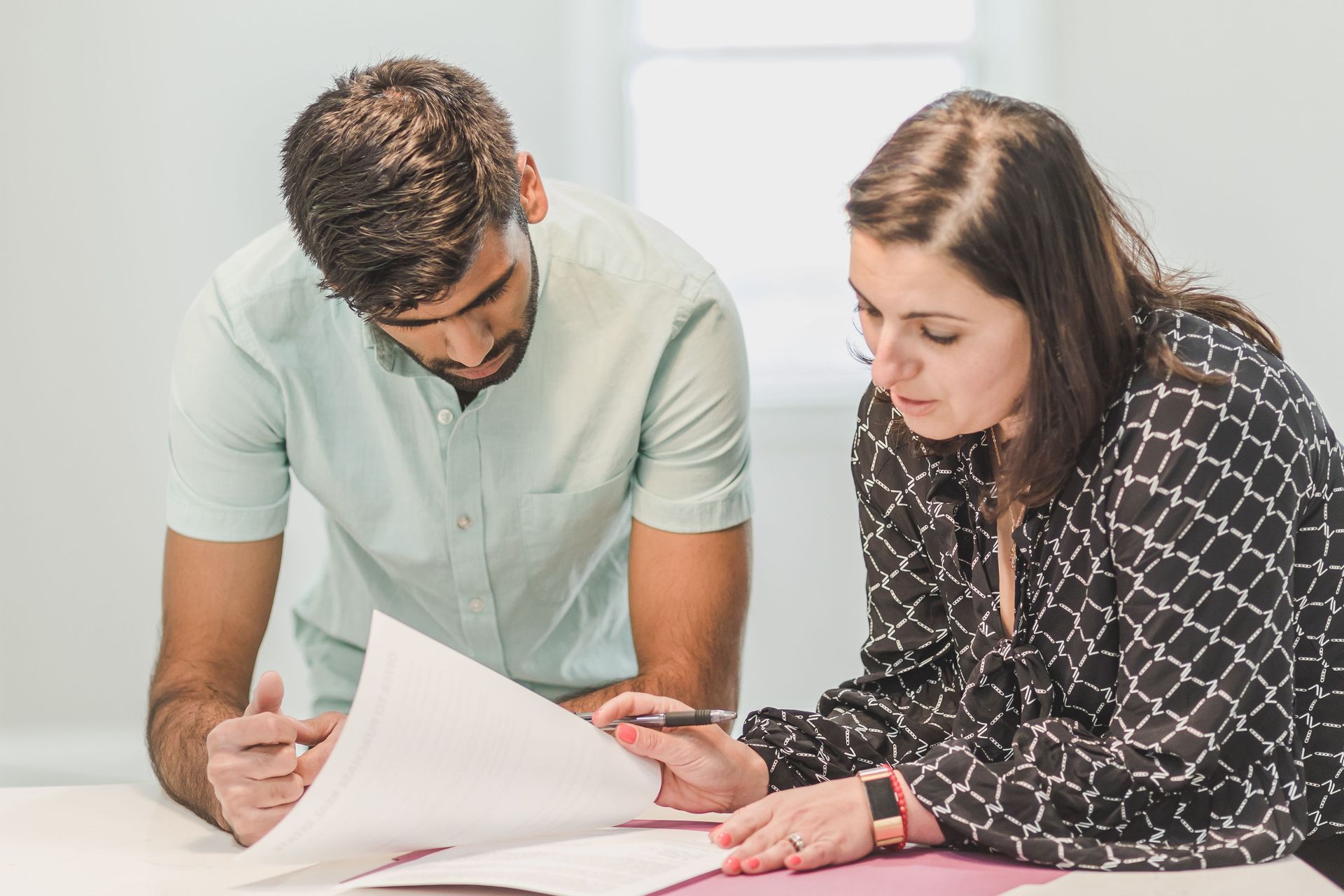 Dois colegas de trabalho revisando documentos juntos em uma mesa em um escritório bem iluminado.