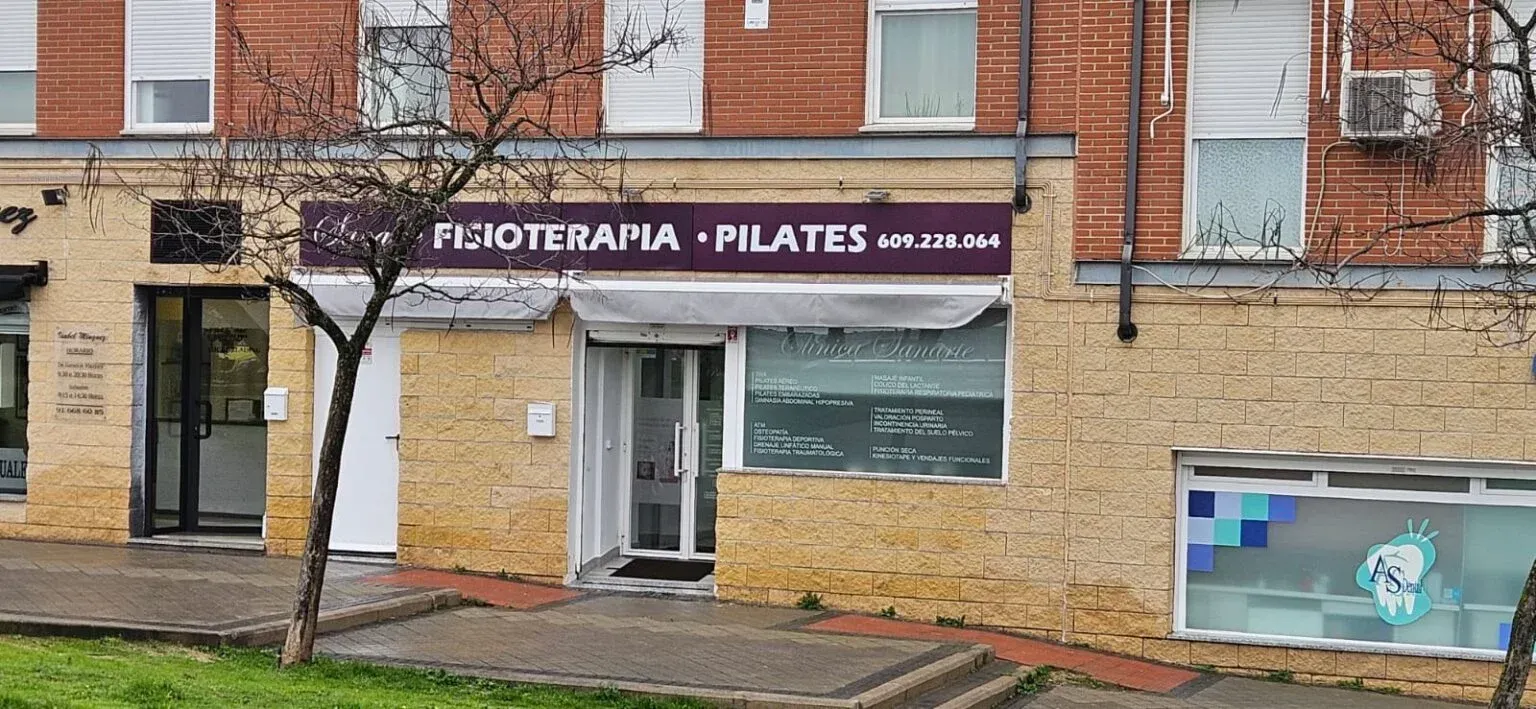 Fachada de un local comercial con un letrero morado que dice “Fisioterapia • Pilates” en un edificio de ladrillo, vista desde la calle.